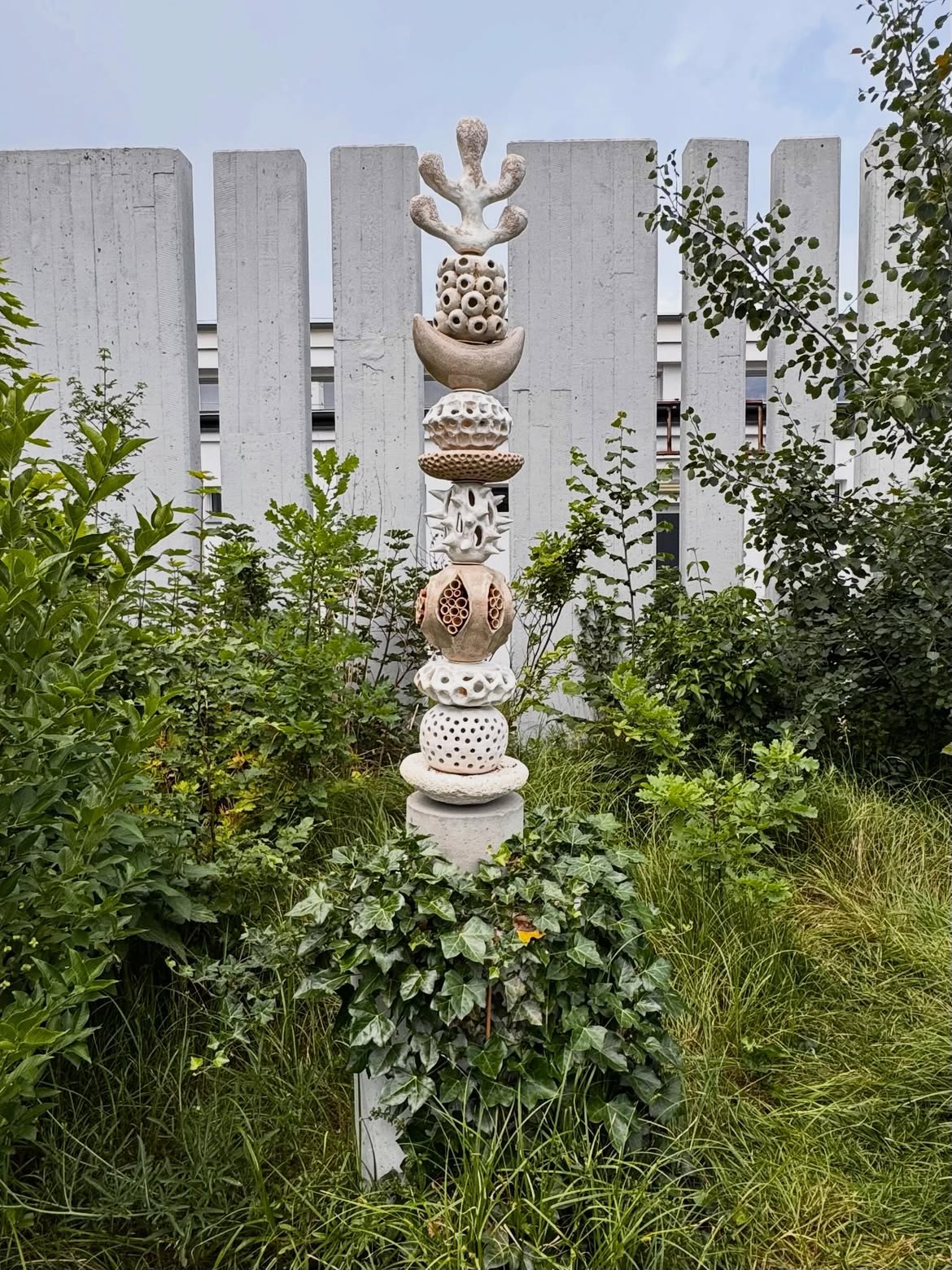 Artistic ceramic insect hotel for wild pollinators, designed as a sculptural totem among garden plants